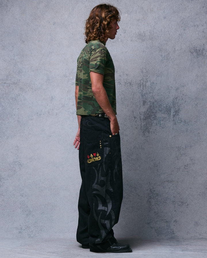 Model wearing wide-leg black jeans, side view showing tribal print down the leg and card-suit embroidered back pocket