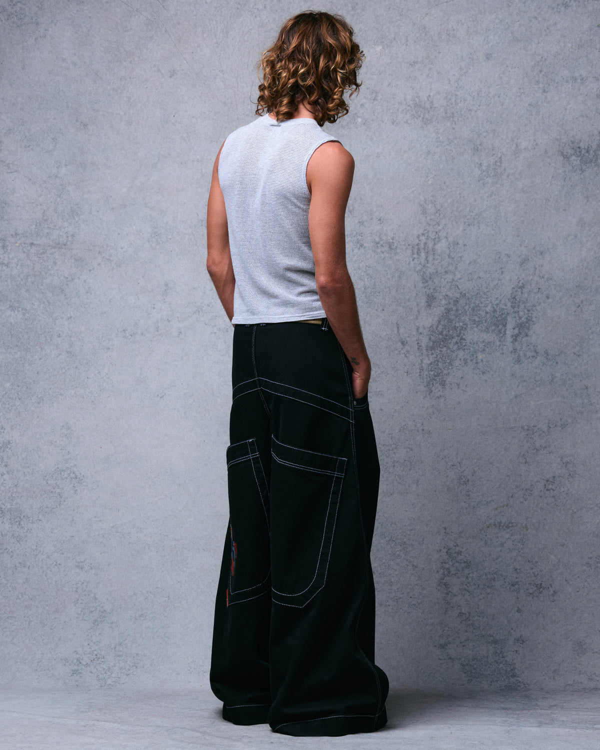 Model wearing black wide-leg jeans with white contrast stitching, three-quarter back view, hand in front pocket