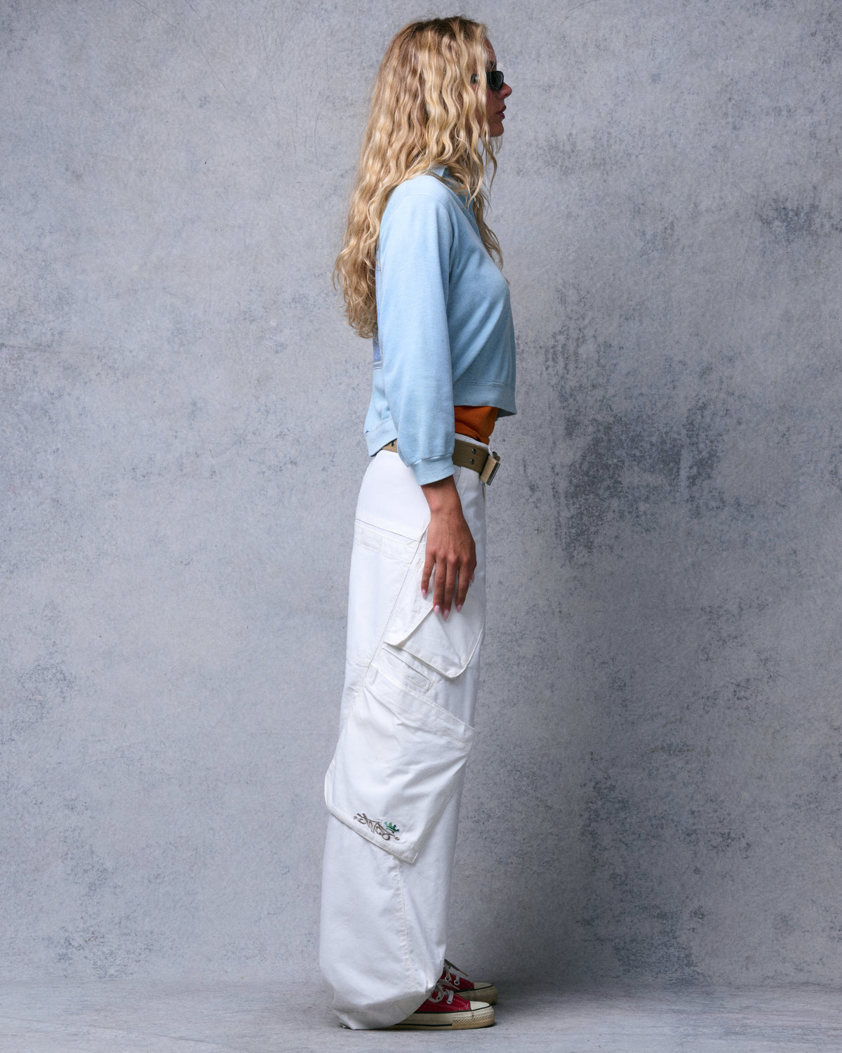 Model in profile wearing wide-leg off-white cargo pants with large side cargo pockets and a tan belt