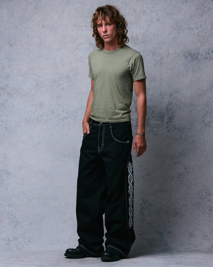 Model wearing wide-leg black jeans with one hand in a front pocket, angled view of the side tribal embroidery