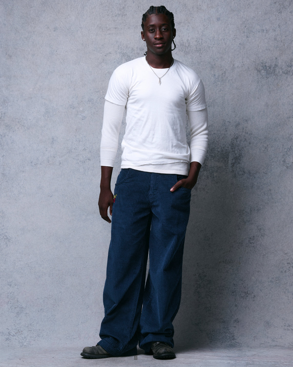 Model wearing navy wide-leg corduroy pants with a white layered top, full-length front view, one hand in pocket