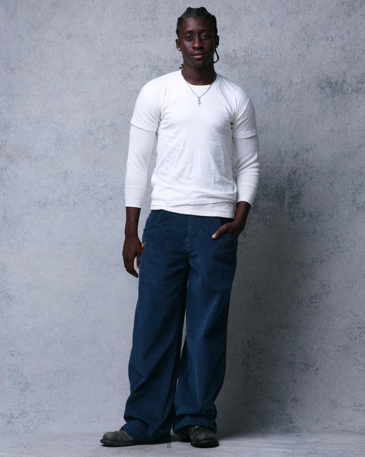 Model wearing navy wide-leg corduroy pants with a white layered top, full-length front view, one hand in pocket