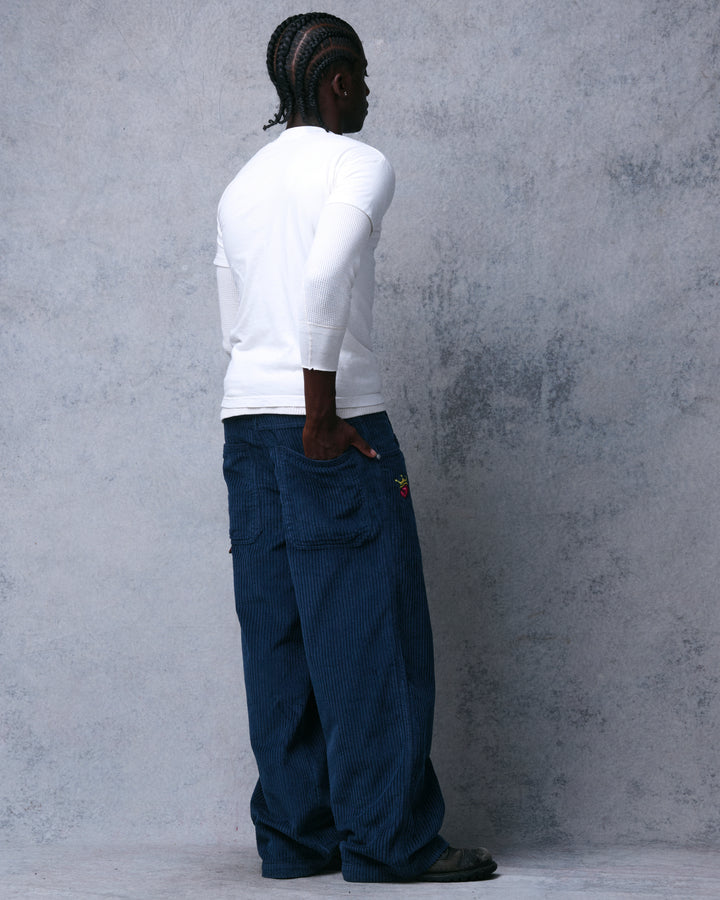 Model wearing navy wide-leg corduroy pants, rear three-quarter view with a hand in the back pocket