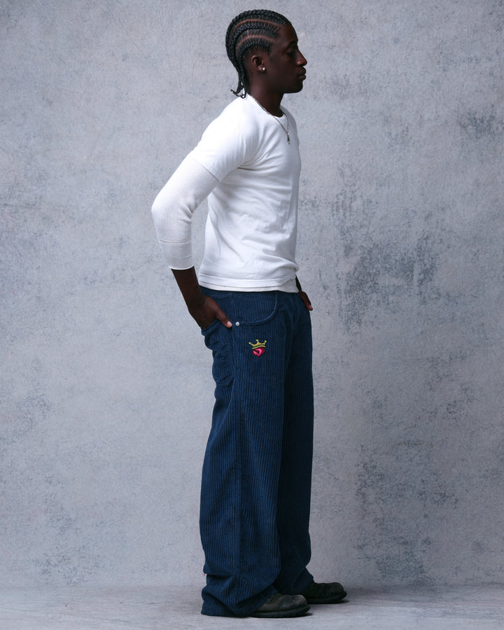 Model wearing navy wide-leg corduroy pants, full-length profile view with crown-and-heart embroidery at the hip