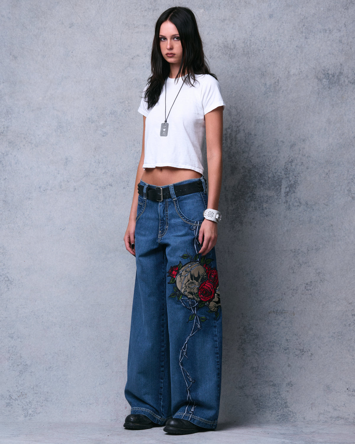 Model in the dark stone wide-leg jeans, front three-quarter full-length view of the skull and rose embroidery and barbed wire