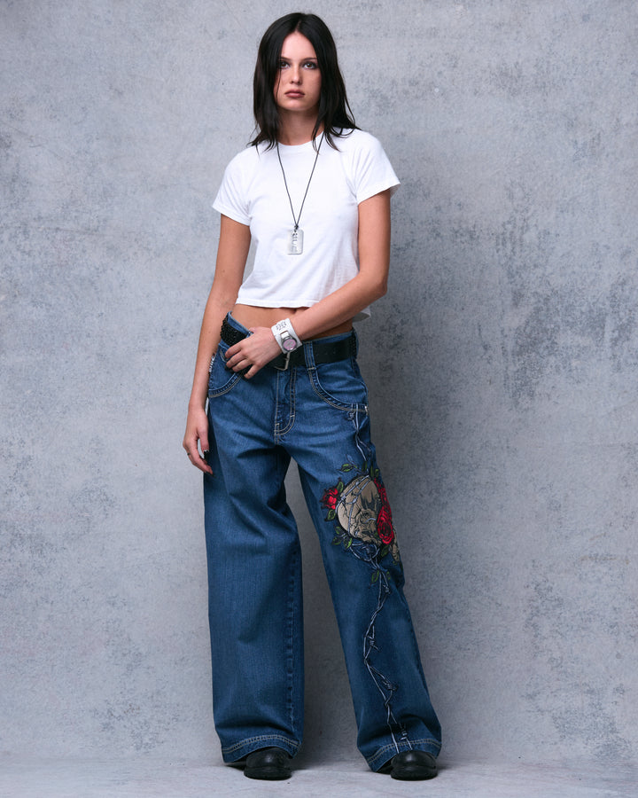 Model in the dark stone wide-leg jeans, one hand at the belt, front view with legs apart showing the full leg embroidery