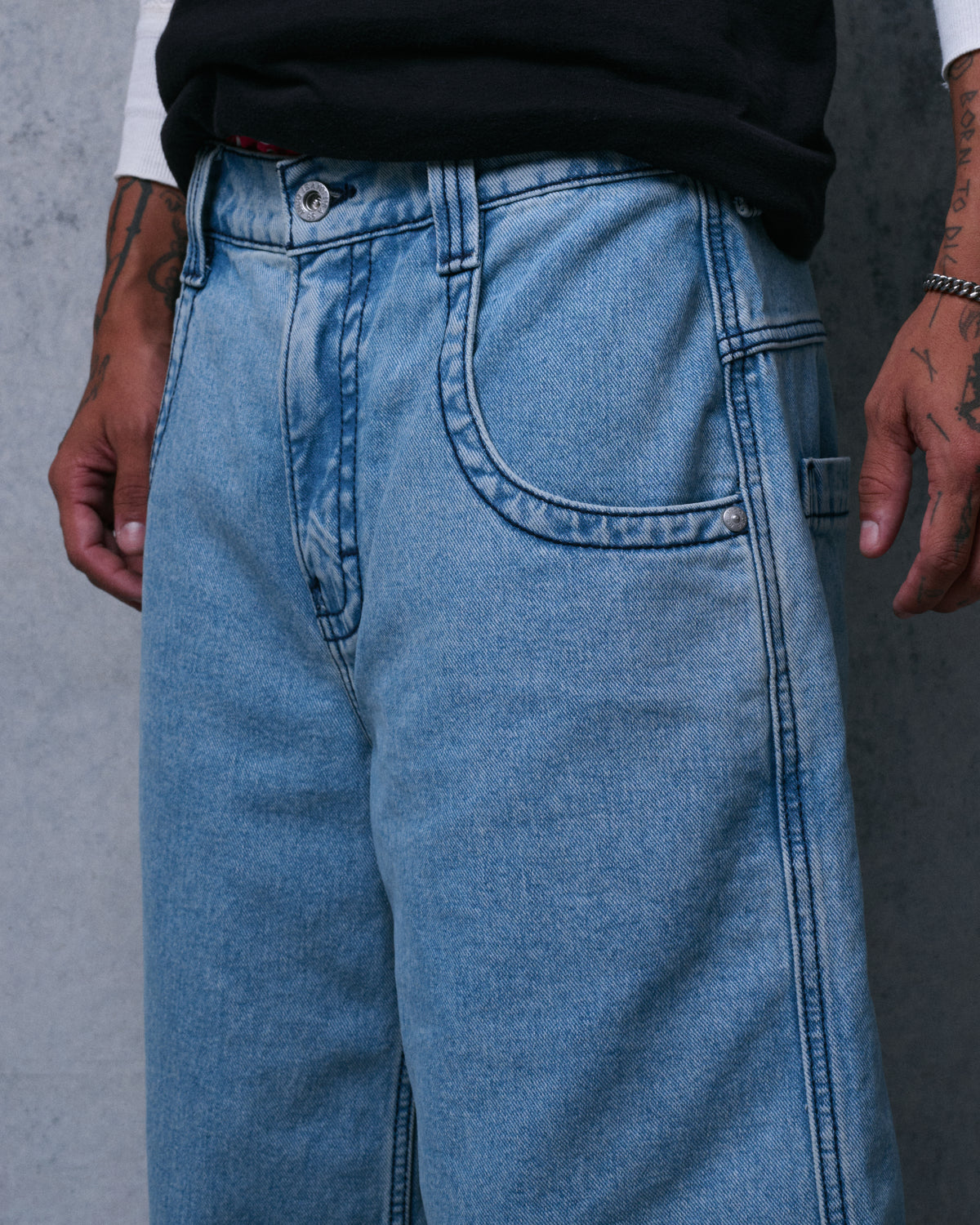 Close-up of the front of light blue denim shorts showing the button fly, front pocket and contrast stitching
