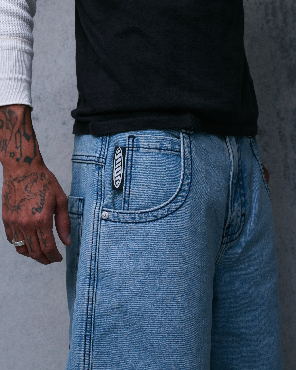 Close-up of the front pocket of light blue denim shorts with a black and white JNCO tab at the pocket edge