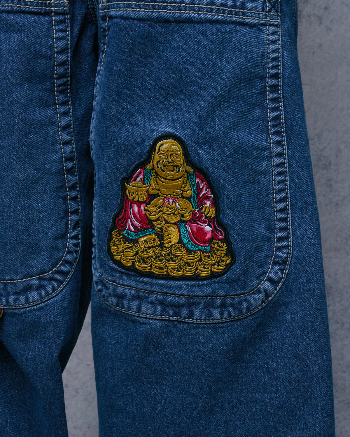Close-up of the embroidered metallic gold Buddha patch on a back pocket of the dark stone wash jeans