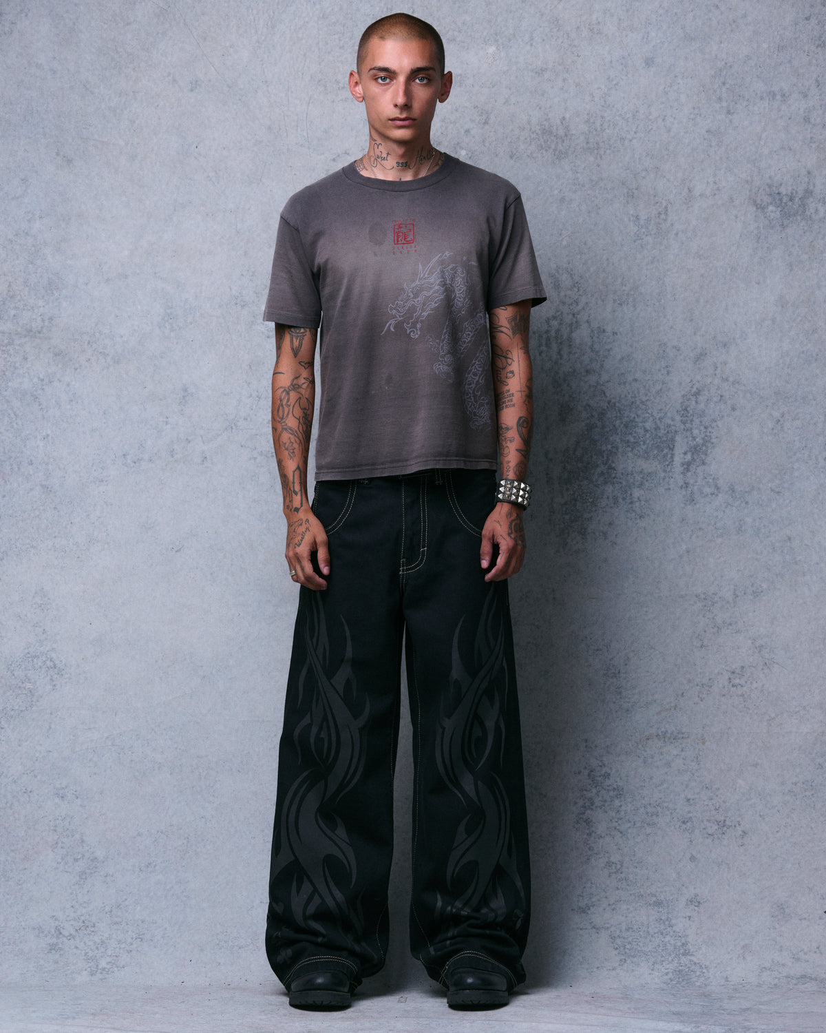 Model wearing black wide-leg jeans with tonal tribal flame print and contrast stitching, front view, full length