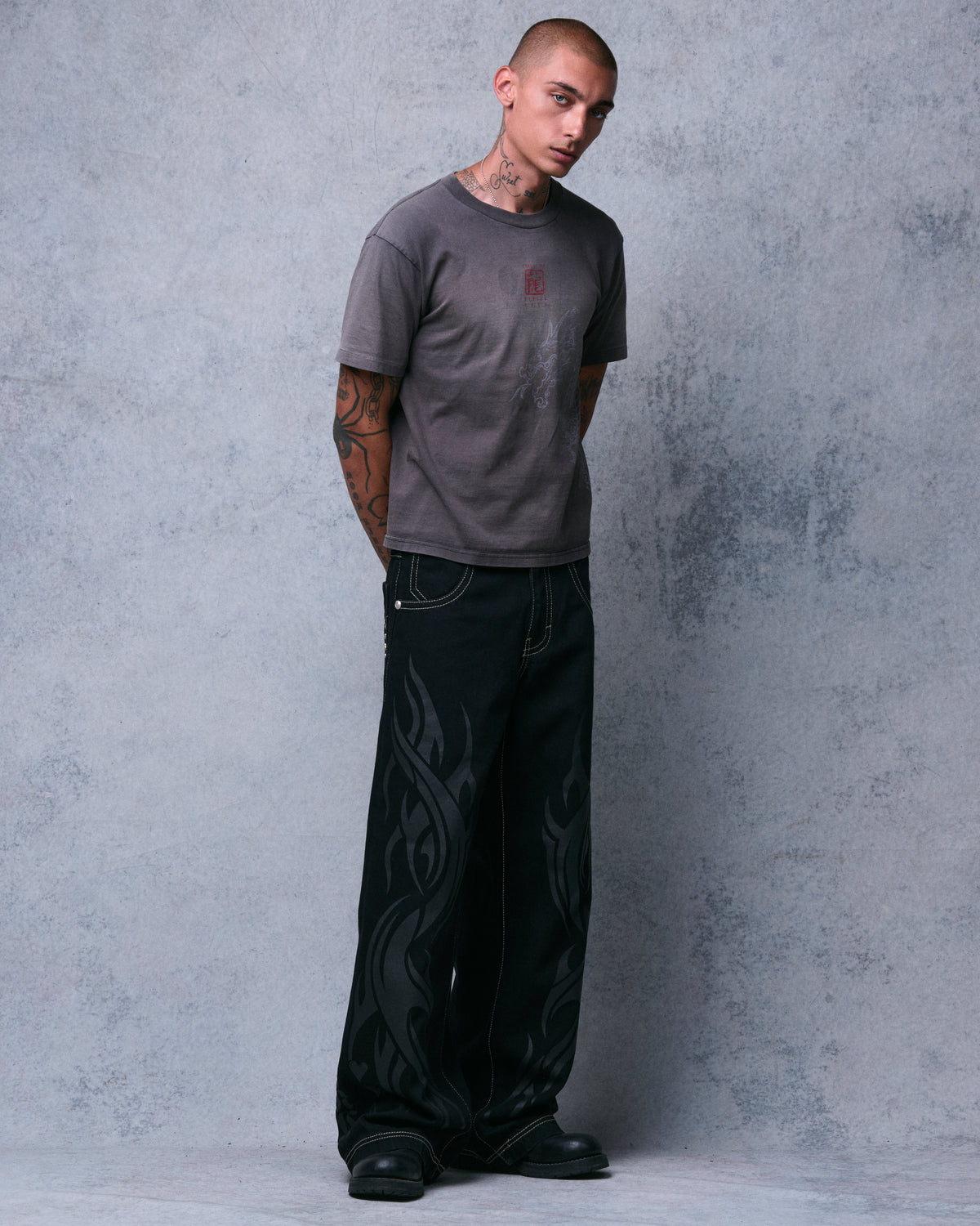 Model in black wide-leg jeans with tonal flame print, three-quarter view from the right, hands behind back