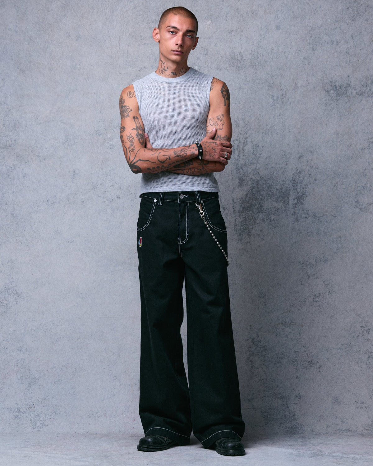 Model with arms crossed wearing wide-leg black jeans with white stitching and a wallet chain, front view