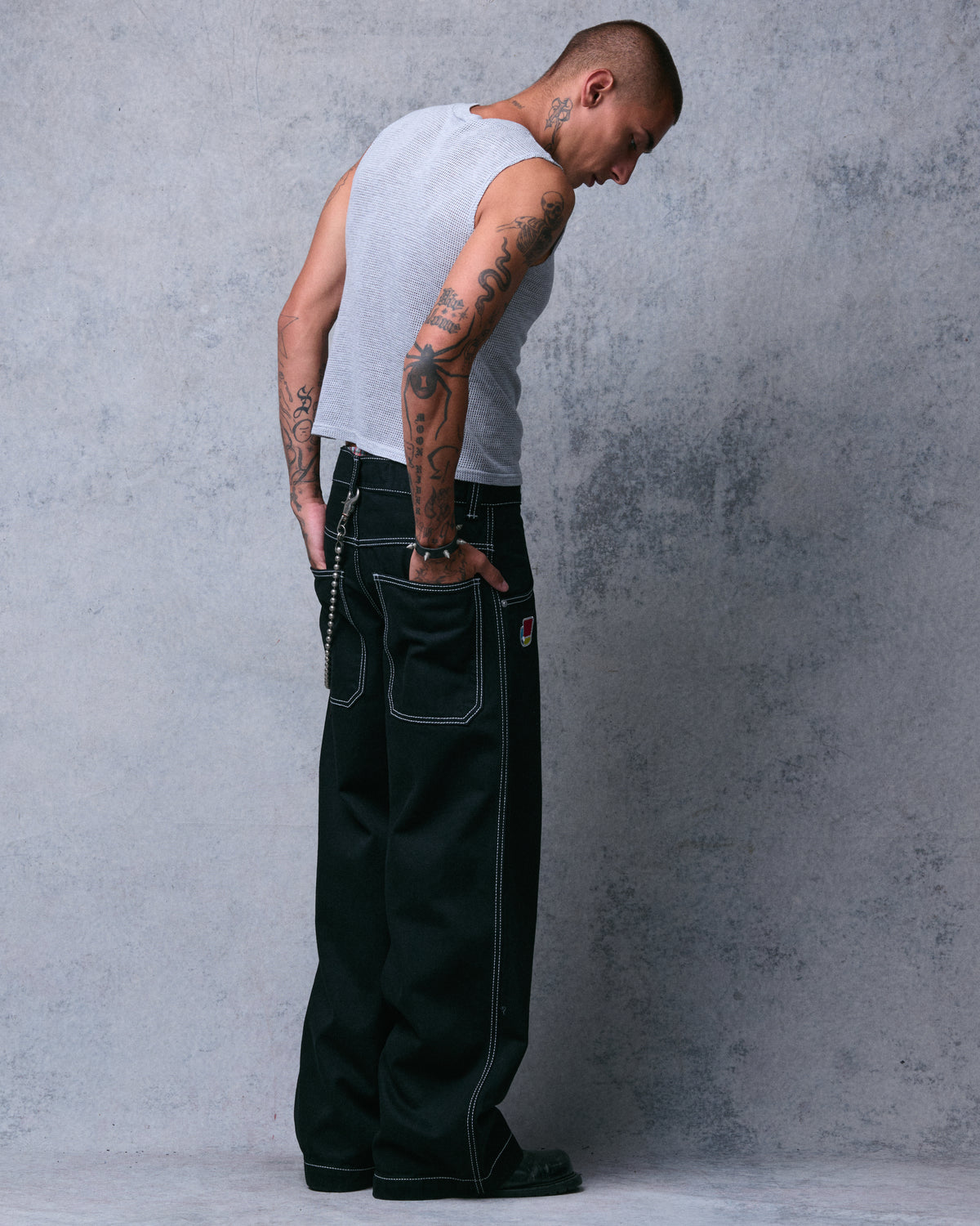 Model in wide-leg black jeans with a wallet chain, back three-quarter view with hands in the back pockets