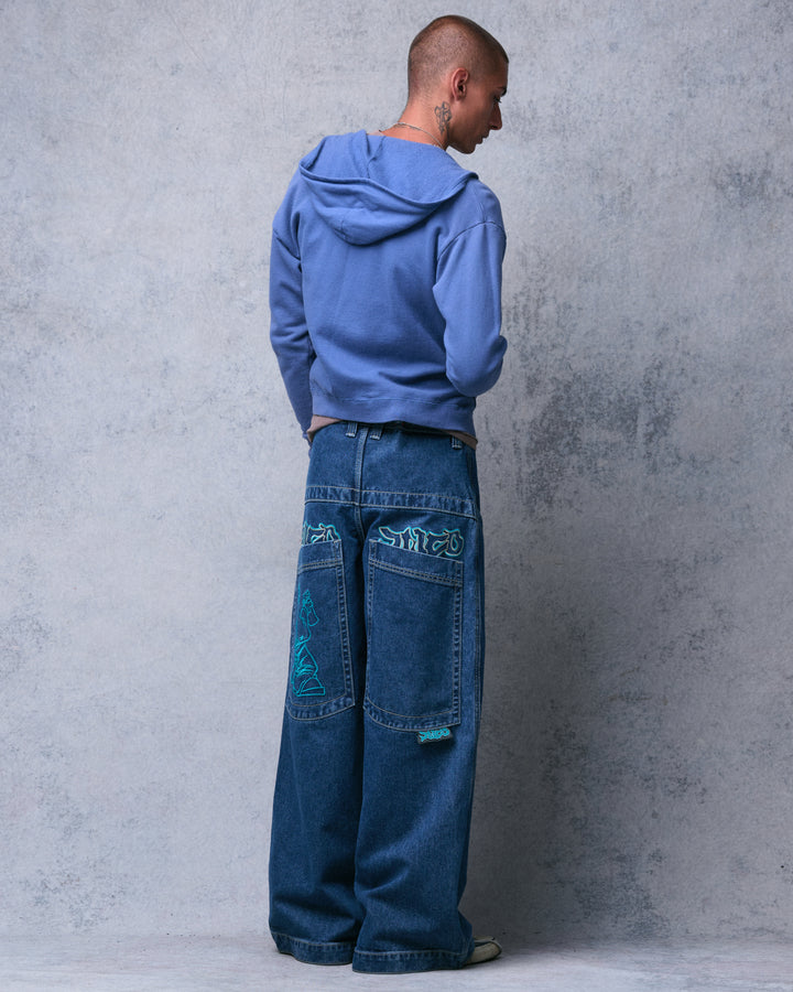 Model wearing the dark stone wash wide-leg jeans, angled back view of the teal embroidered pockets and logo tab