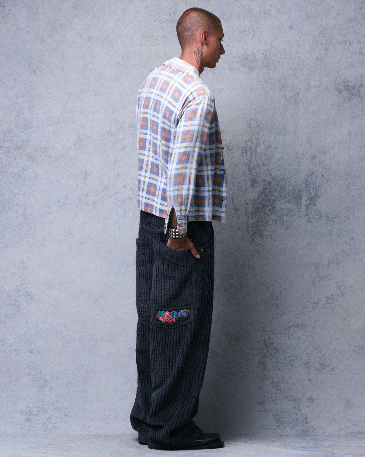 Rear three-quarter view of the dark charcoal corduroy pants with hand in back pocket above the embroidered logo
