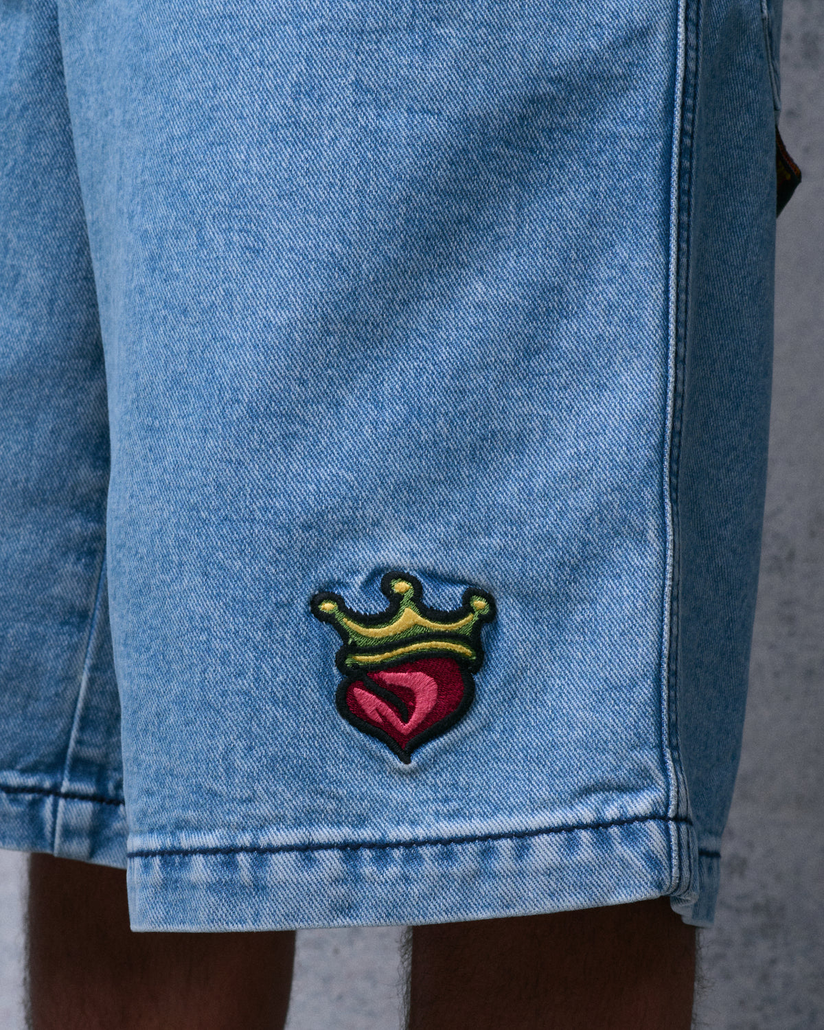Close-up of the shorts' leg showing the embroidered red heart with gold crown and the stitched hem