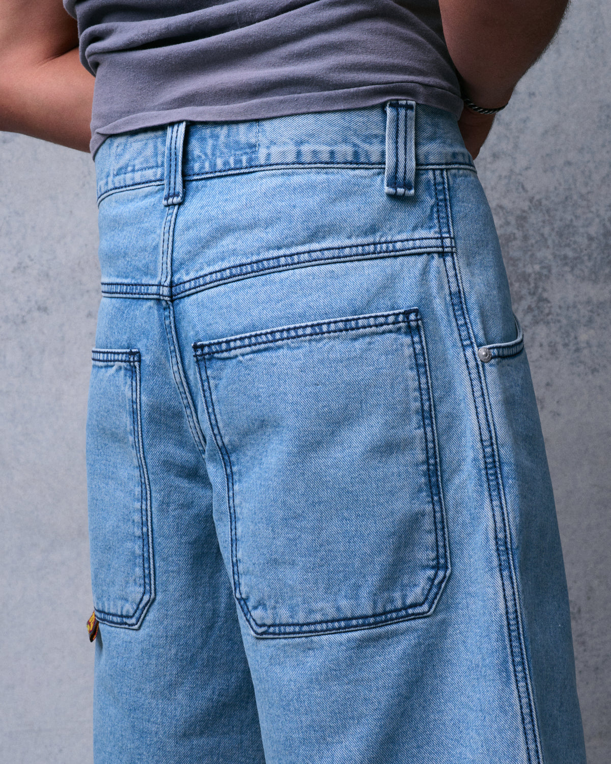 Back view close-up of light blue denim shorts on a model, showing belt loops, yoke and large back pockets