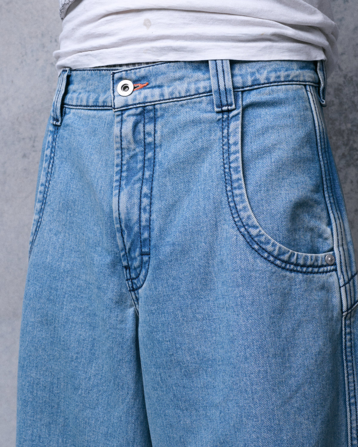 Close-up of the front of light blue jeans showing the button, fly and front pocket with contrast stitching