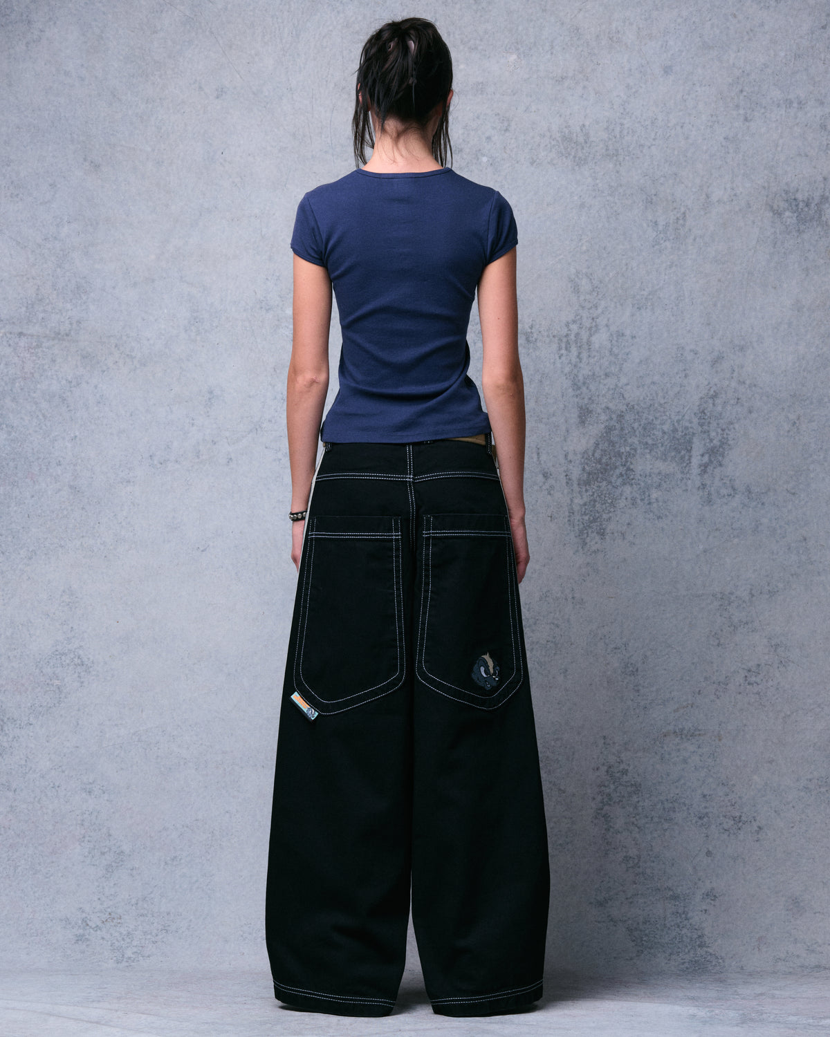 Model wearing jet black wide-leg jeans, back view showing large stitched back pockets and a skunk face patch