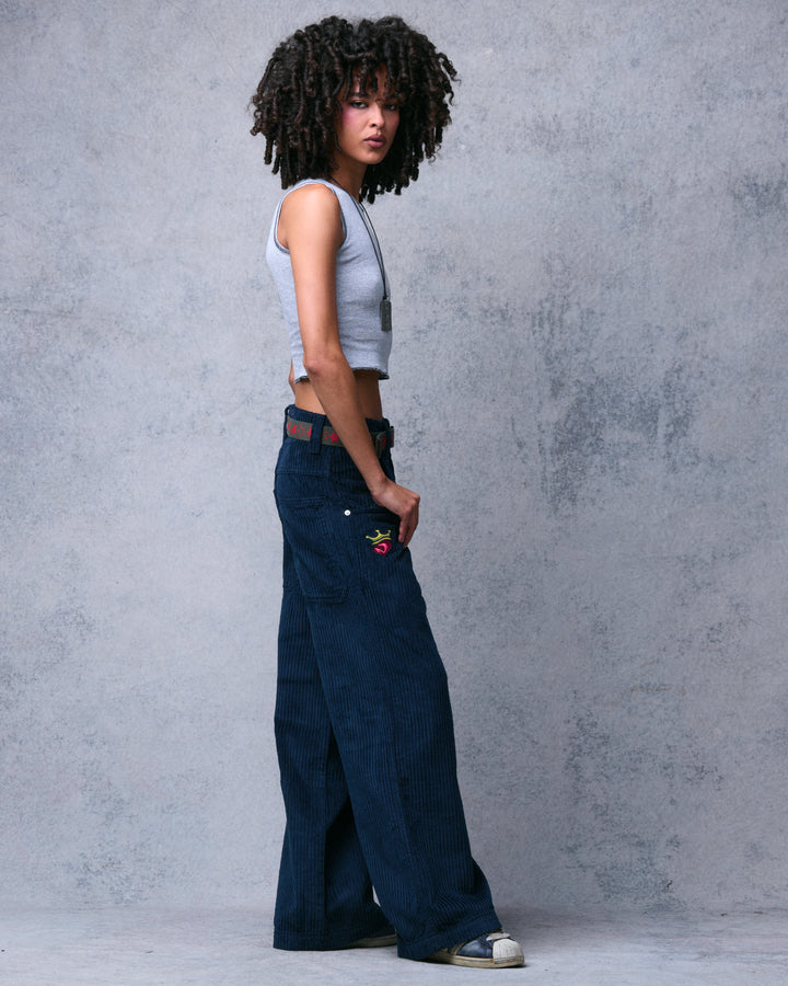 Model wearing navy wide-leg corduroy pants, side view looking back, showing the crowned heart patch