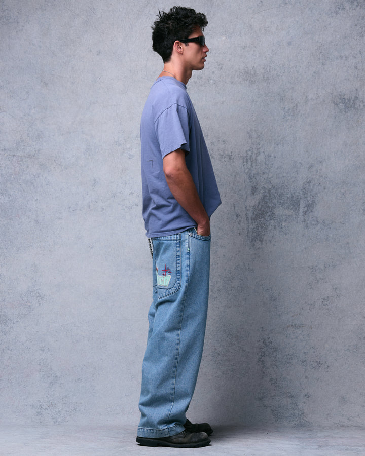 Model wearing light blue antique wash wide-leg jeans, side profile showing the embroidered back pocket