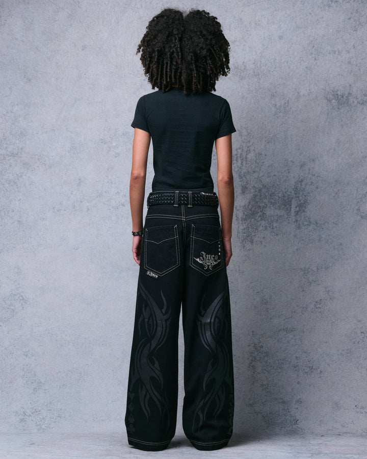 Model wearing black wide-leg jeans, full back view showing silver Jnco pocket embroidery and tonal flame print