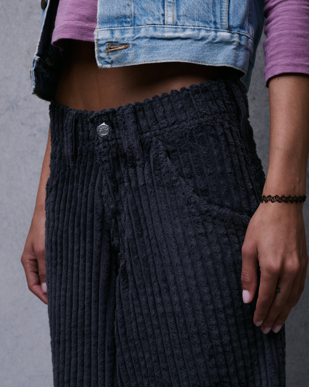 Close-up of the corduroy pants' front waistband, metal button and front pocket on a model