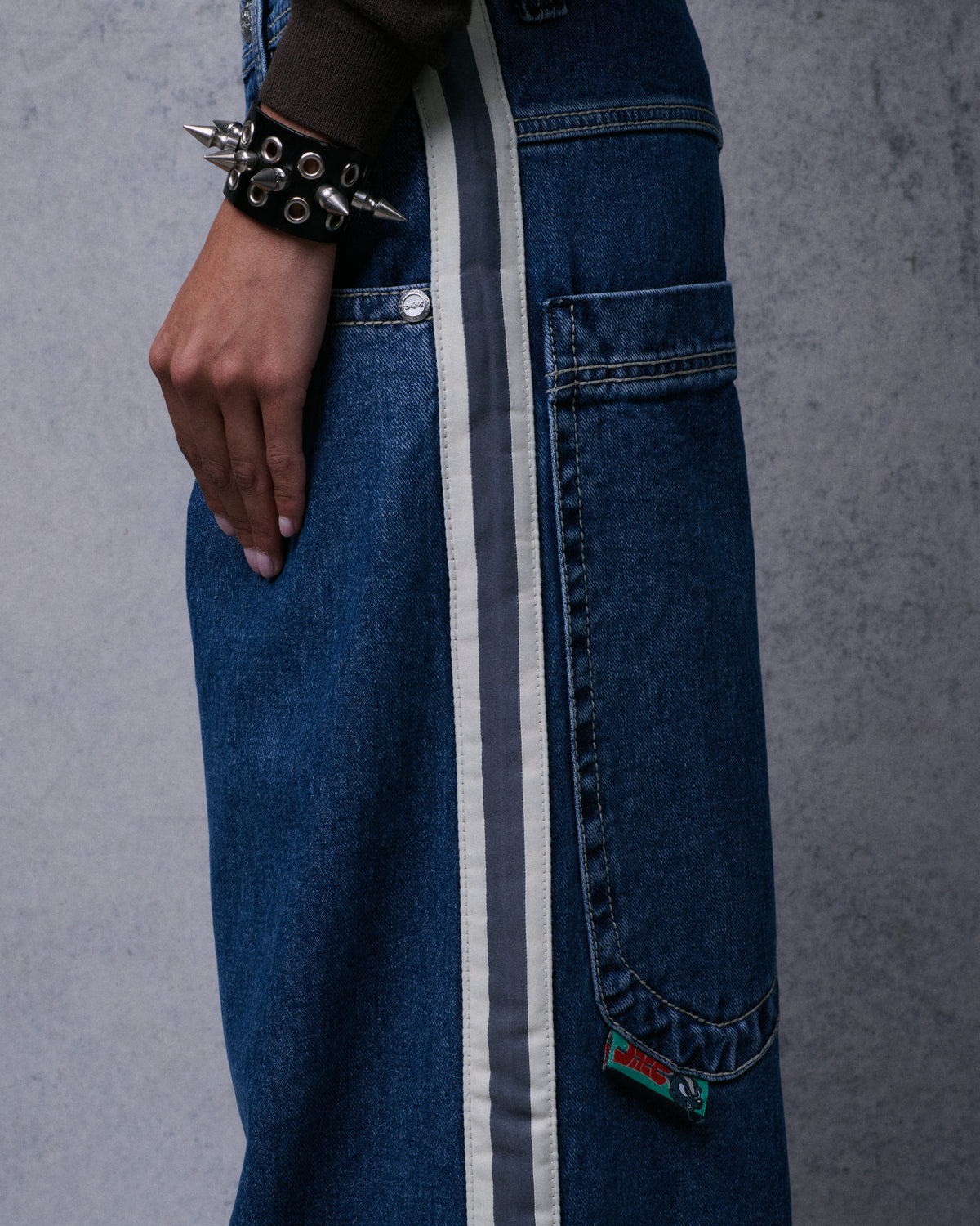 Close side view of dark stone wide-leg jeans with natural and charcoal leg tape beside a back pocket and flasher tag