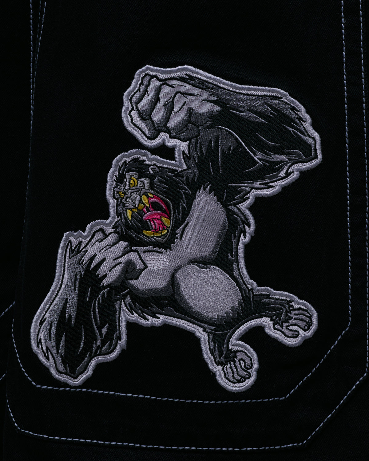 Embroidered patch of a roaring gray and black gorilla with a raised fist on a black denim back pocket