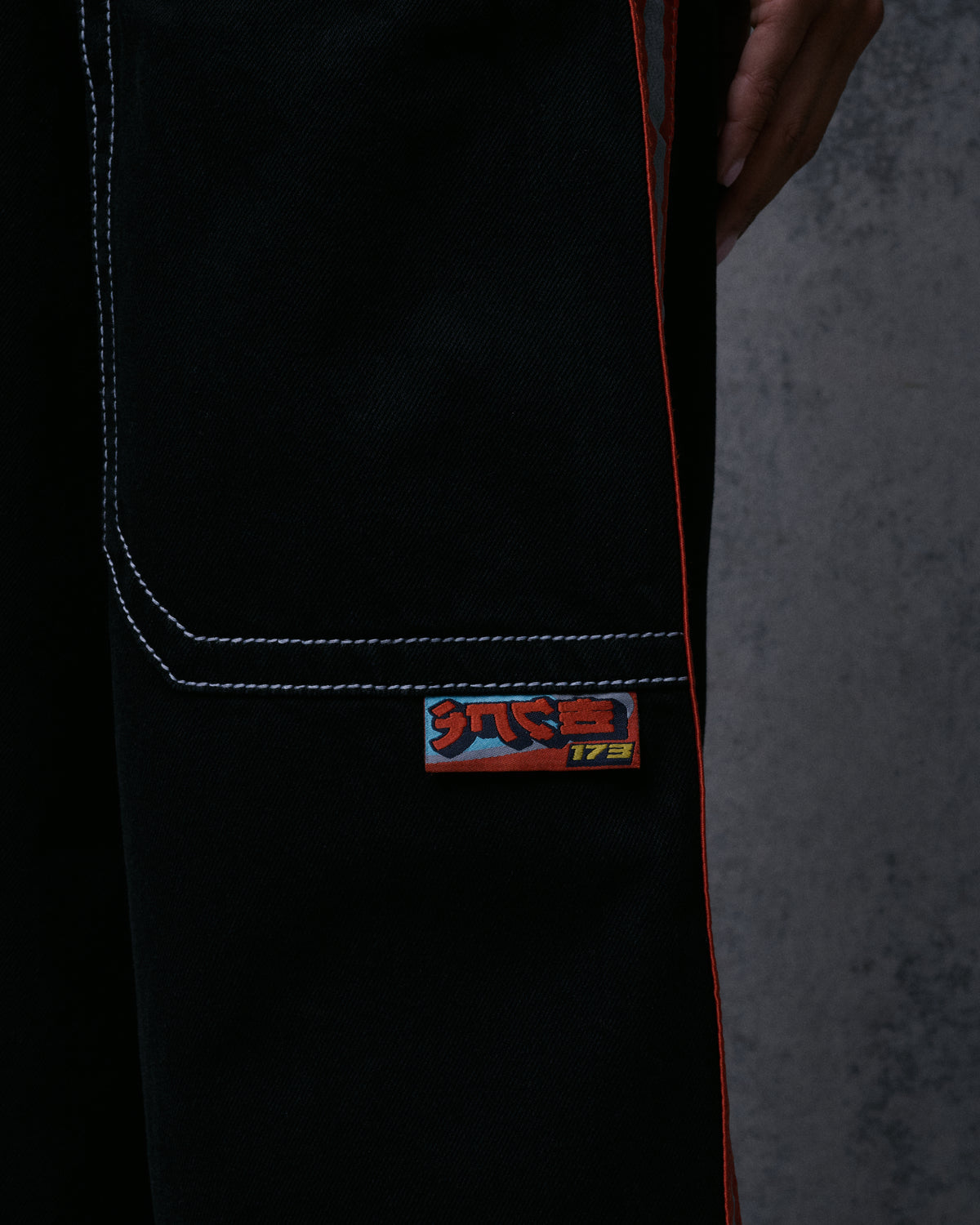 Close-up of a woven JNCO-style label below a back pocket, with orange side stripe along the leg