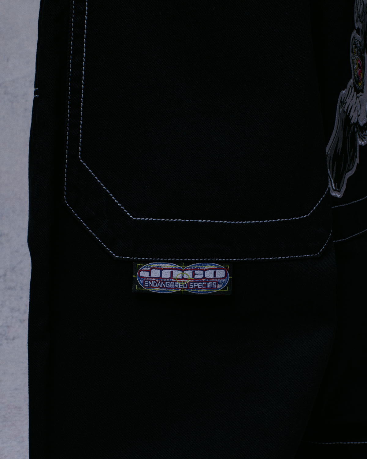 Close-up of a black jeans back pocket with a JNCO Endangered Species woven label below it