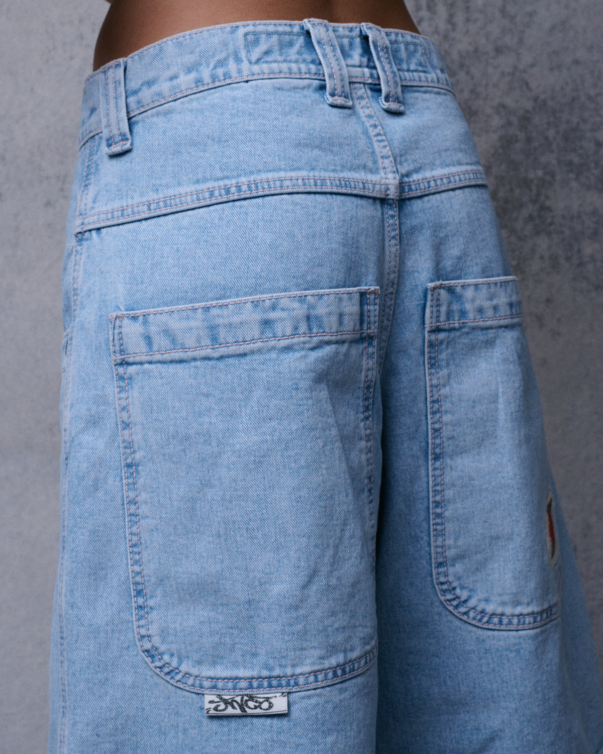 Close-up of light-wash denim shorts from the back at an angle, showing large patch pockets and a small woven tag