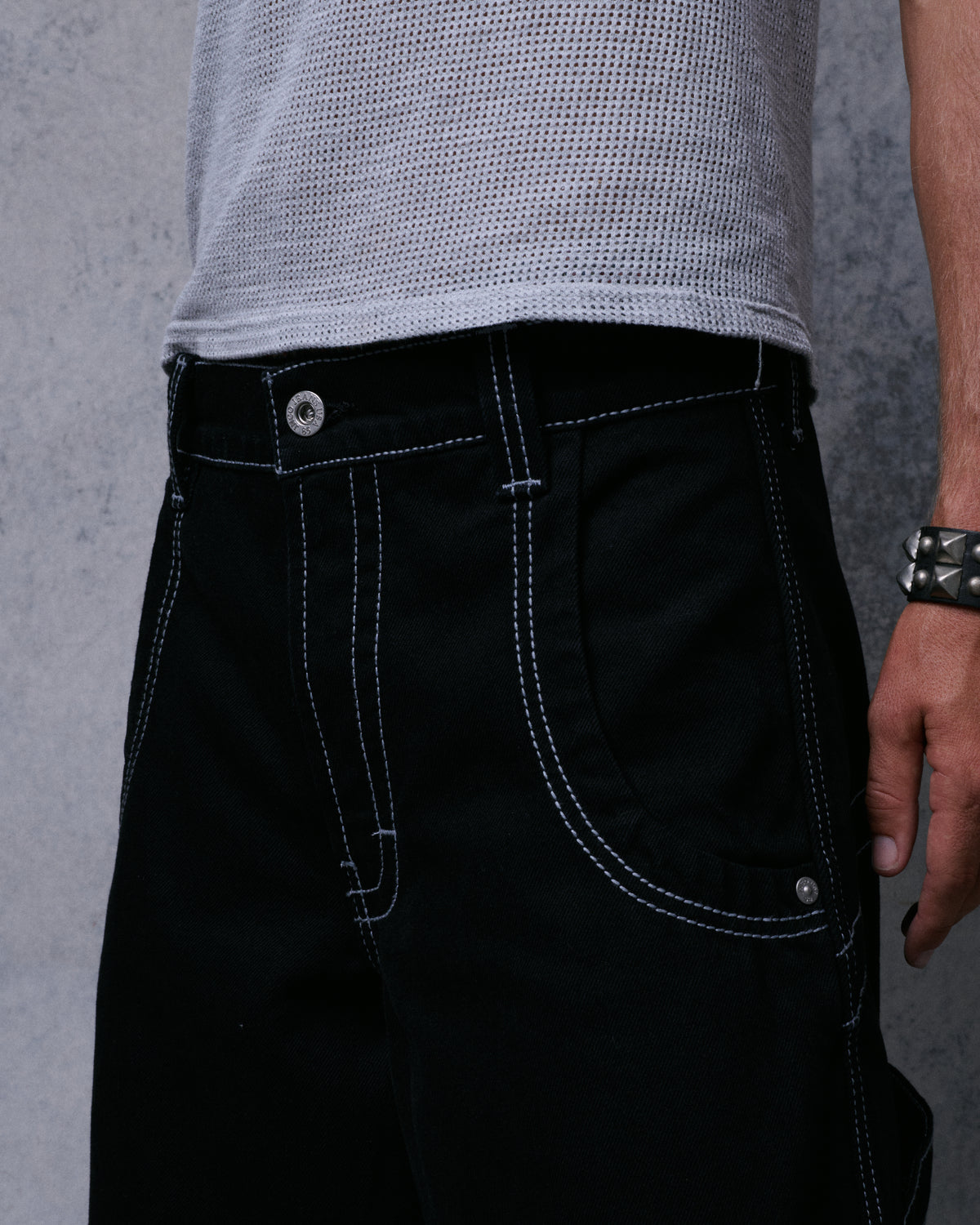 Close-up of black jeans front waistband, button, fly and front pocket with white double stitching
