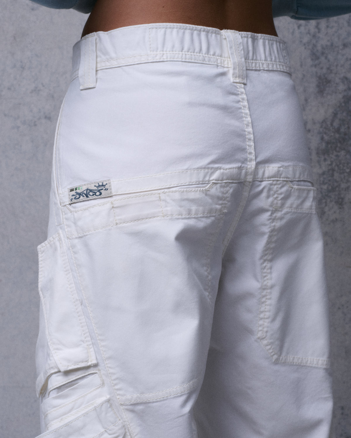 Close-up of the back waistband and pocket of off-white cargo pants on a model, three-quarter rear view with small JNCO tab