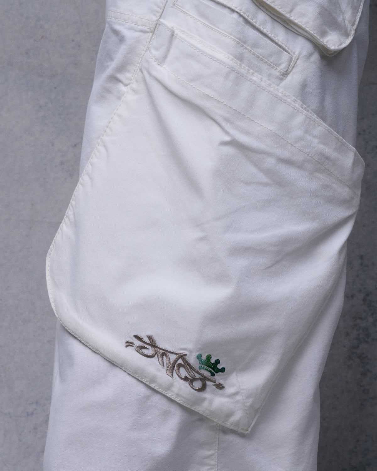 Close-up of an off-white cargo pocket with embroidered JNCO script logo and green crown
