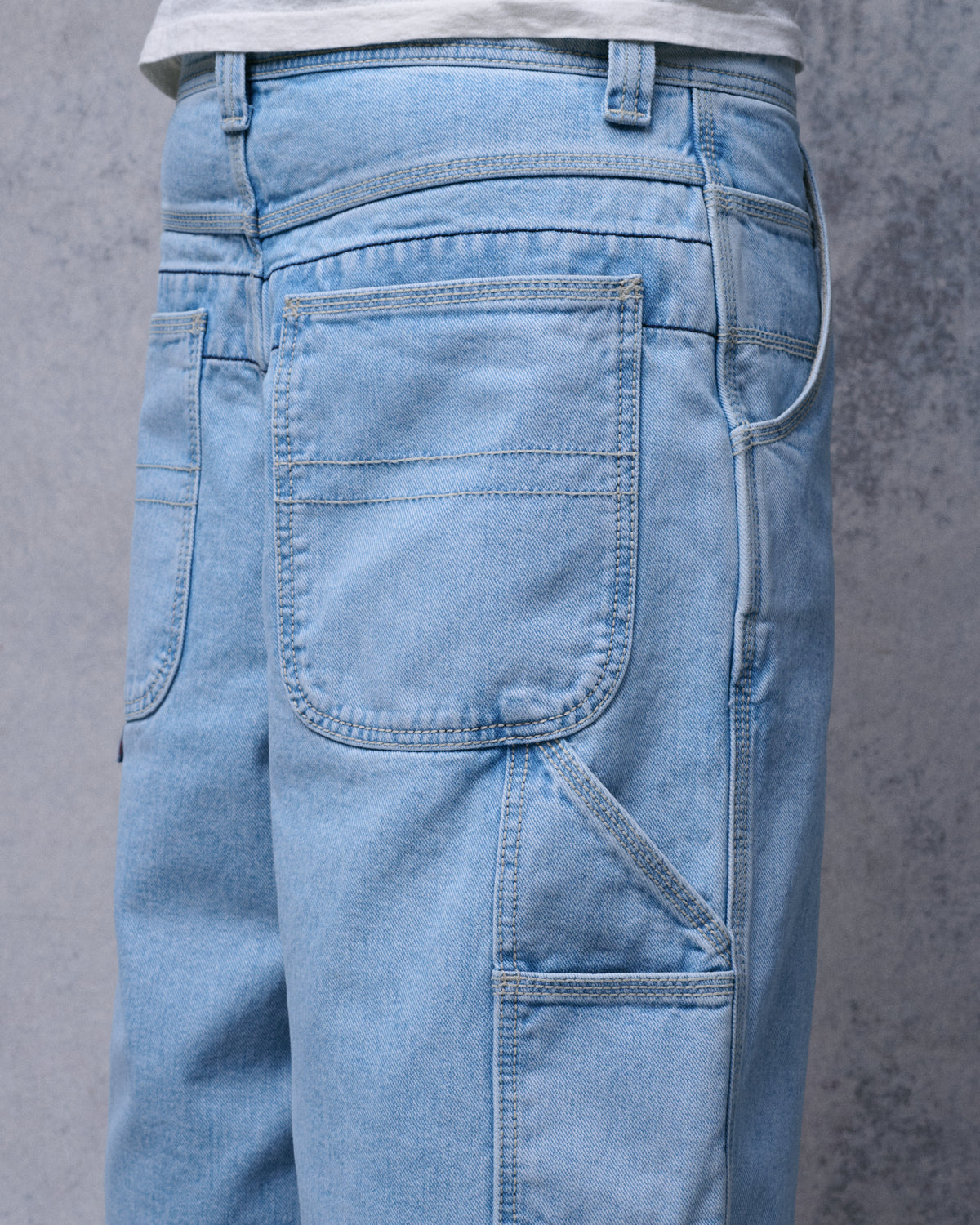 Back and side view of light-wash carpenter shorts on a model, showing the rear patch pocket and side utility pockets