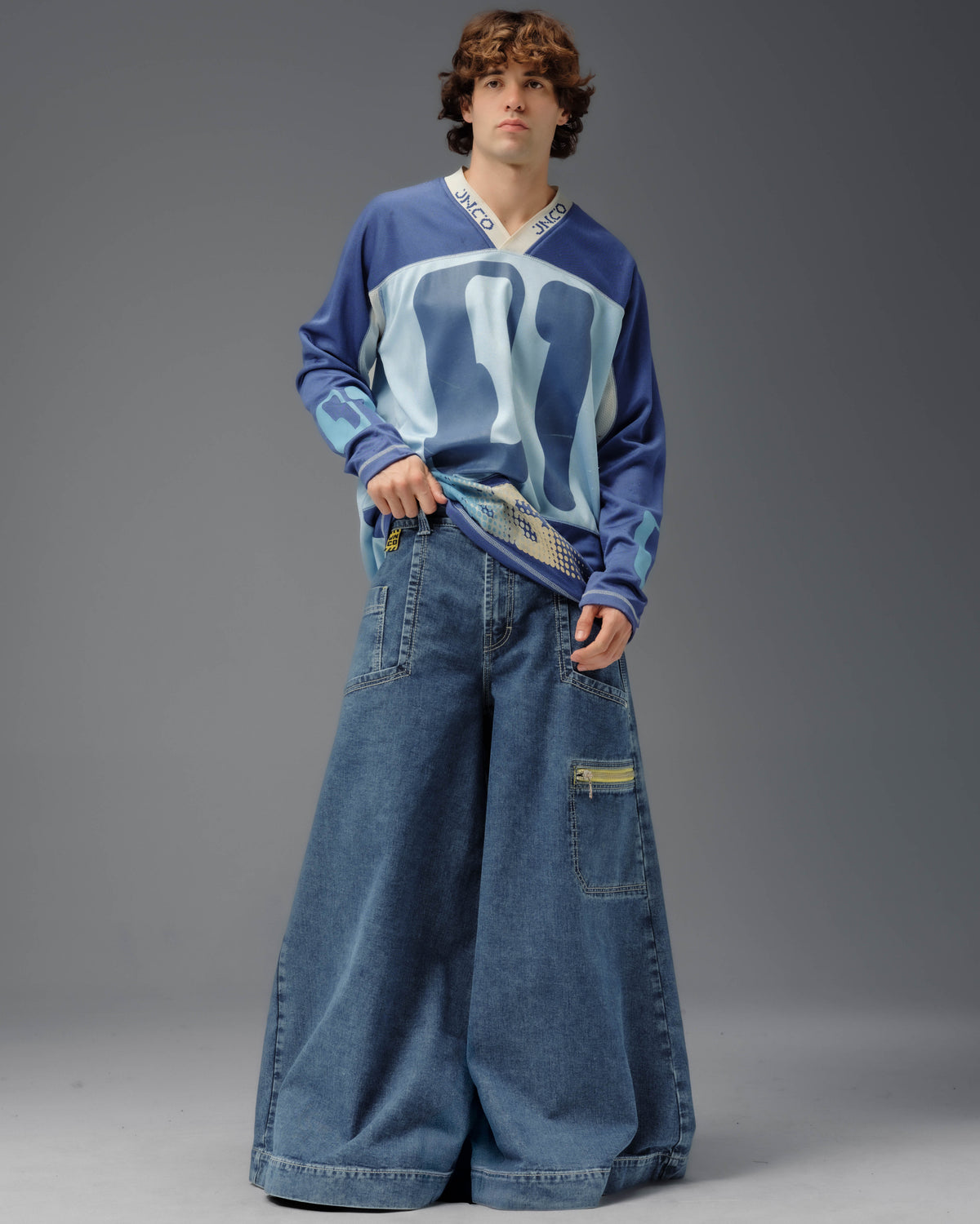 Model wearing extremely wide blue JNCO jeans with oversized utility pockets and sports jersey