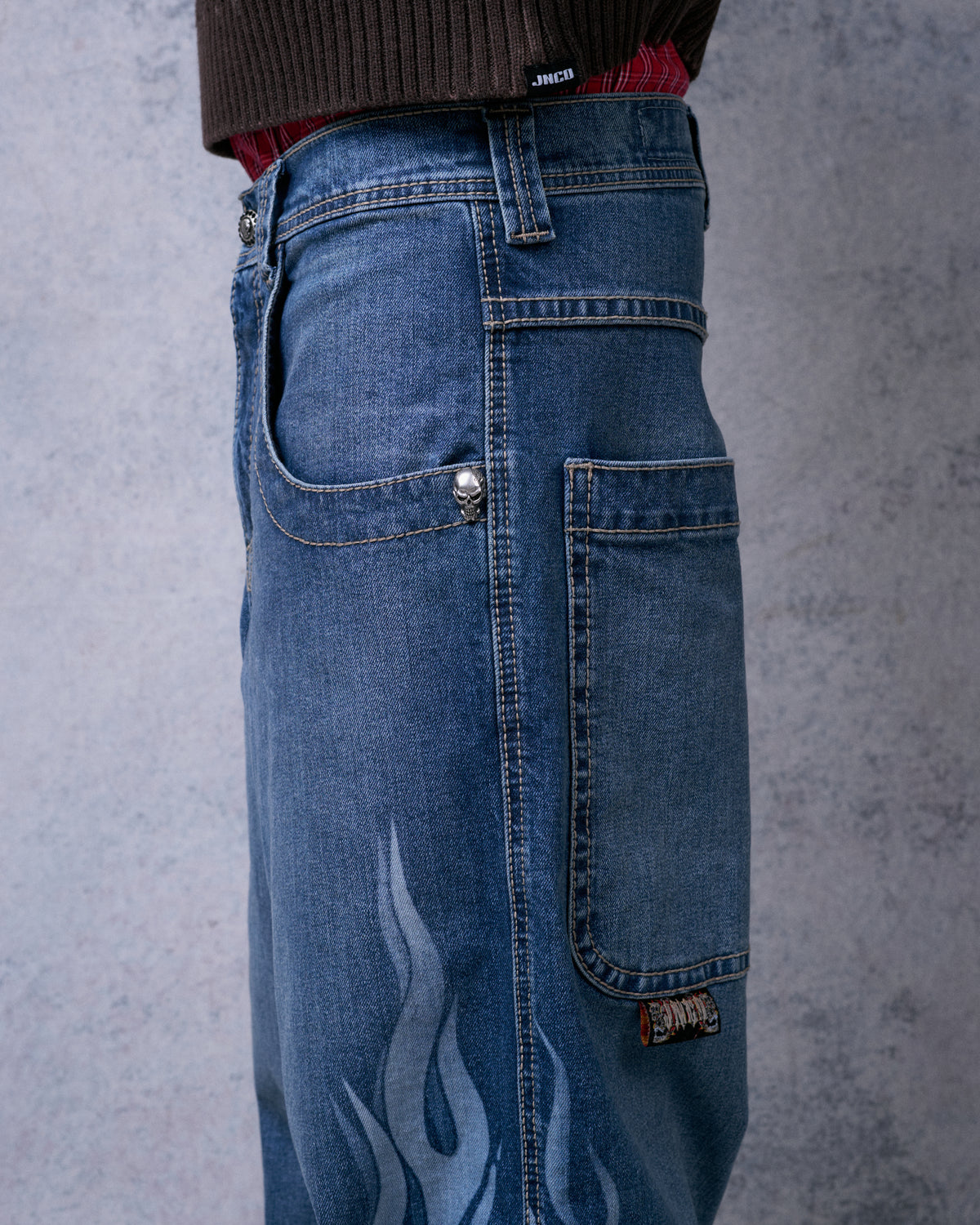Close-up side view of the jeans showing skull rivet, side pocket with woven label, and flame print on the leg