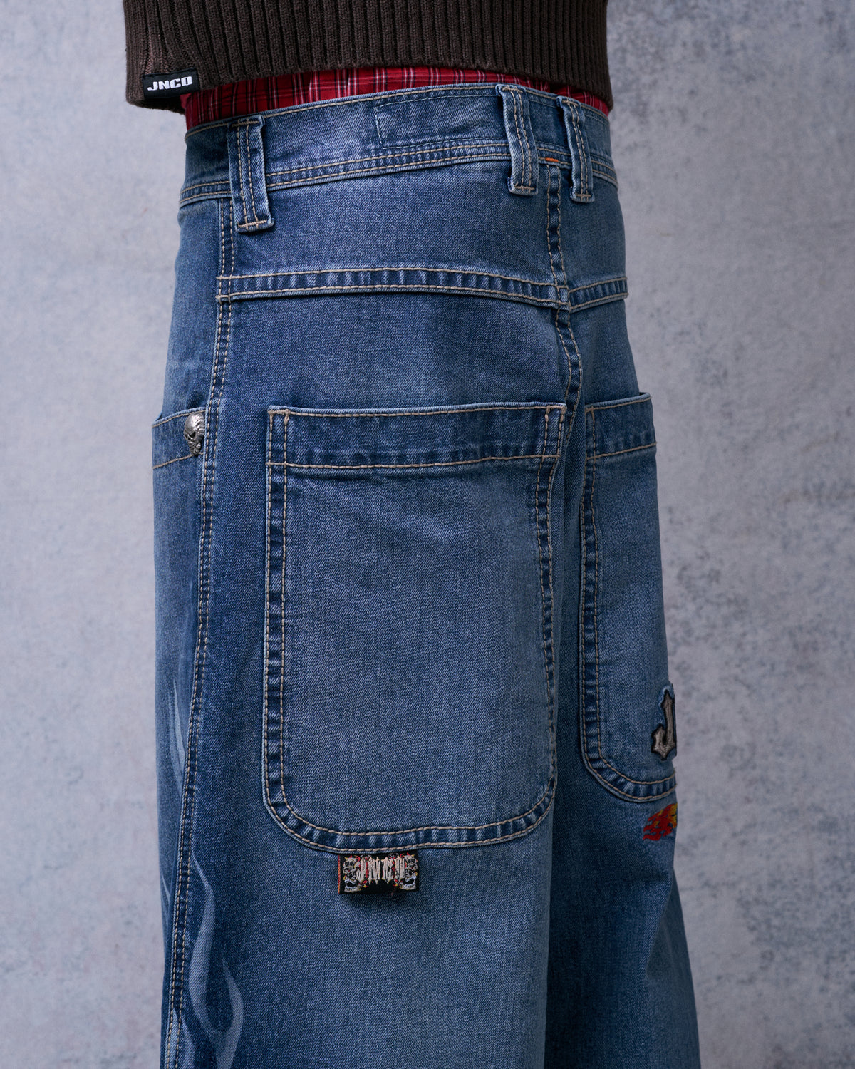 Close-up back view of the jeans showing large back pocket with woven label, skull rivet, and embroidery