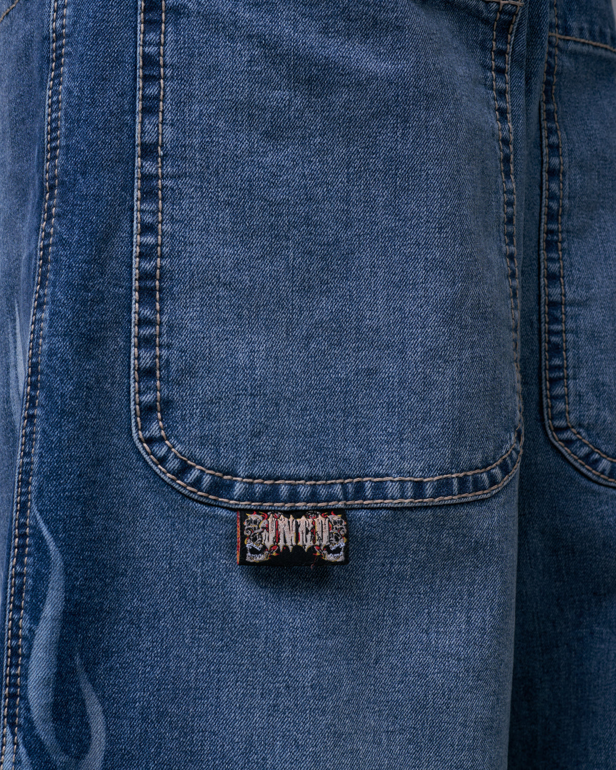 Close-up of a front pocket on blue denim jeans with contrast stitching and a small skull tab label below it