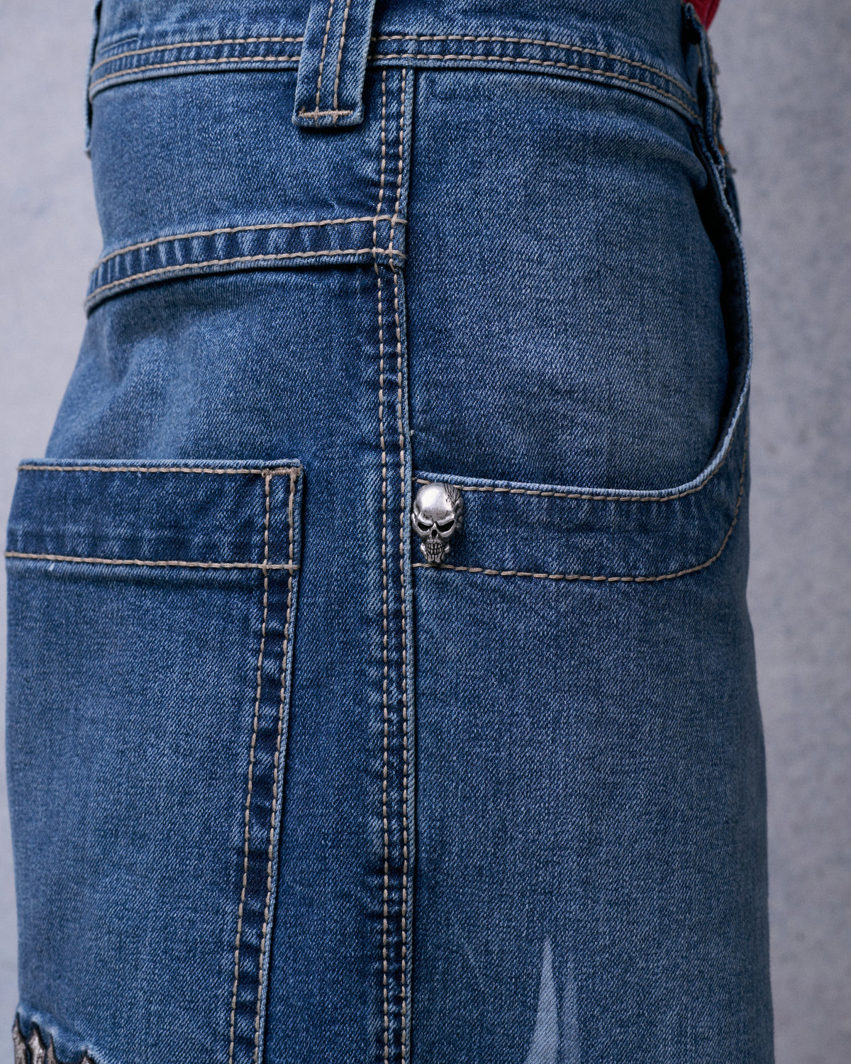 Close-up of the jeans' side and back pockets with contrast stitching and a silver skull rivet