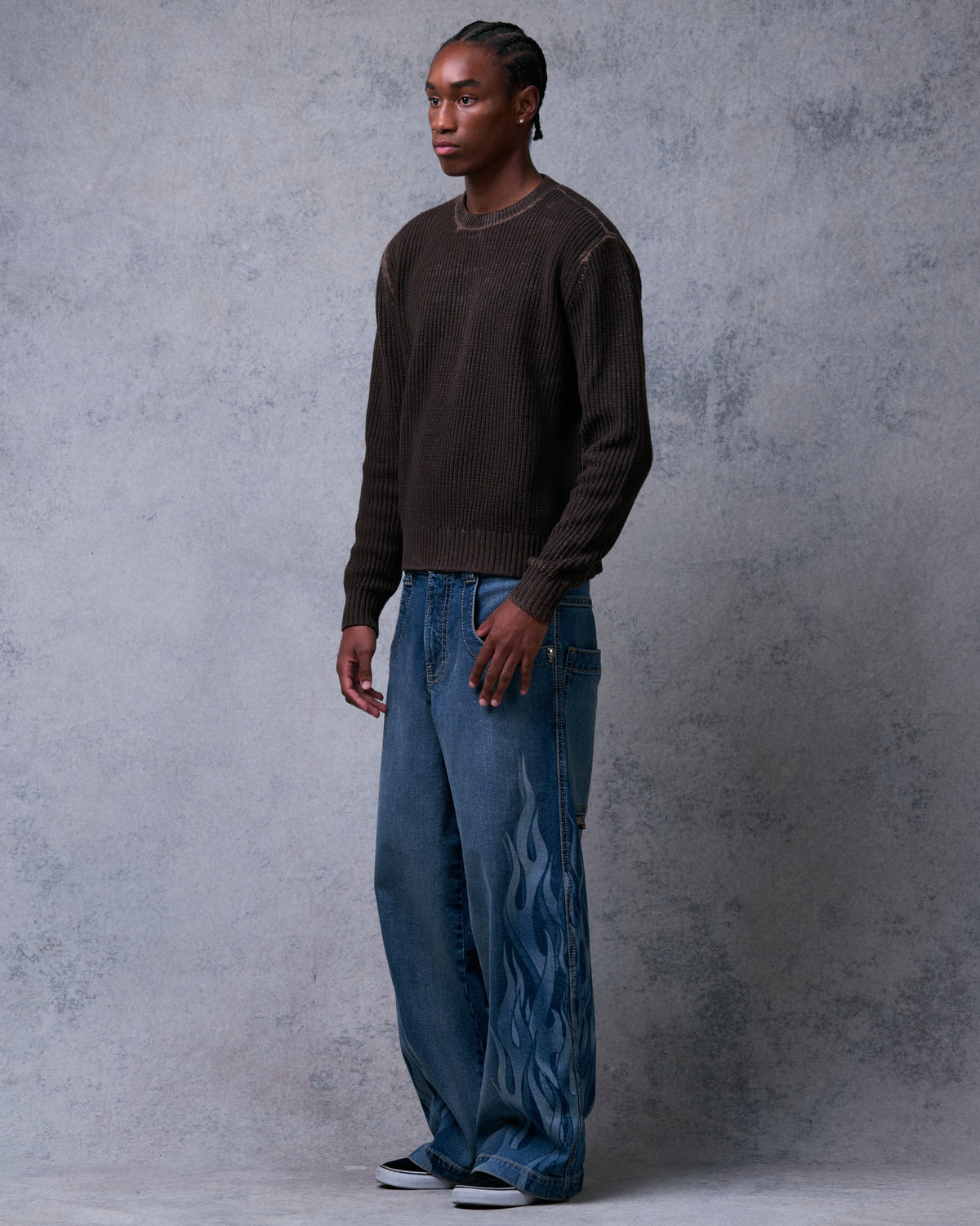 Model wearing wide-leg blue jeans with tonal flame print, front three-quarter view, hand in front pocket