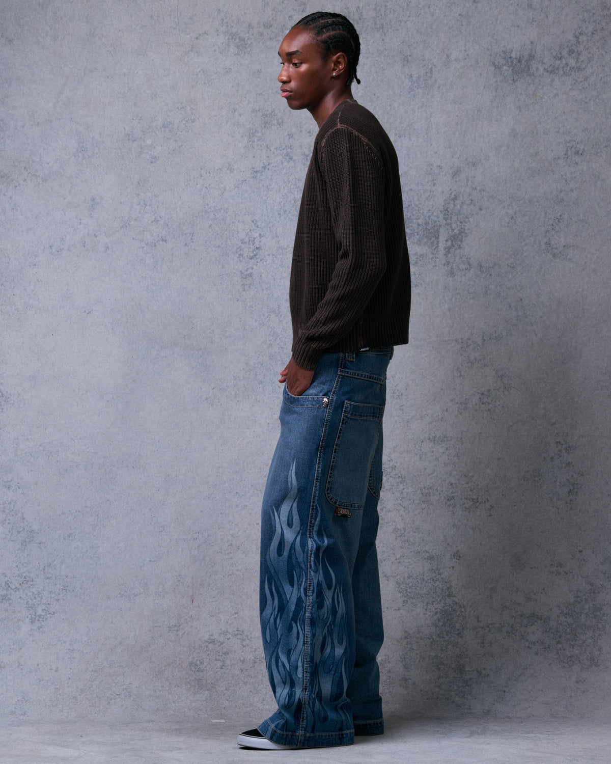 Model wearing wide-leg blue jeans, side view showing flame print running down the leg and side pocket