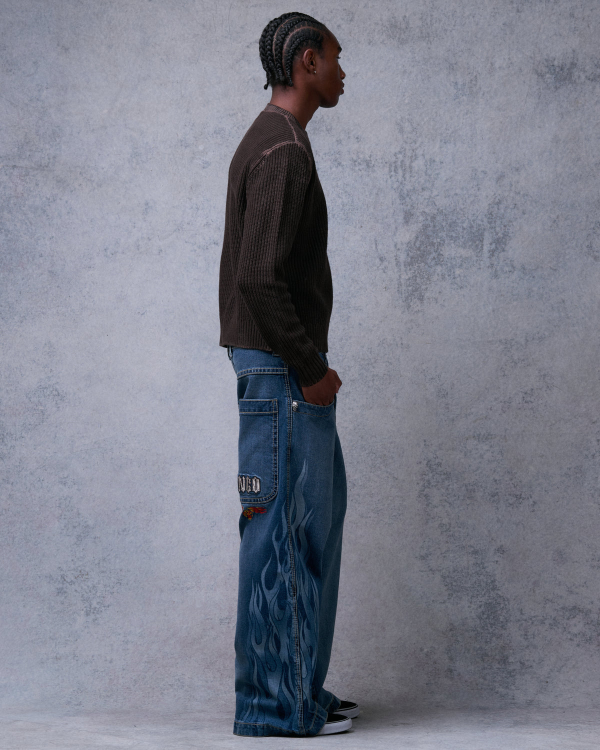Model wearing wide-leg stone wash jeans with tonal flame print down the leg, side view, hand in front pocket