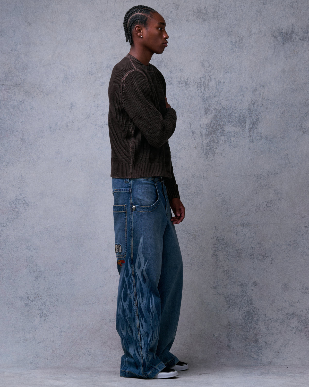Model wearing wide-leg stone wash jeans with tonal flame print, side view with arms folded