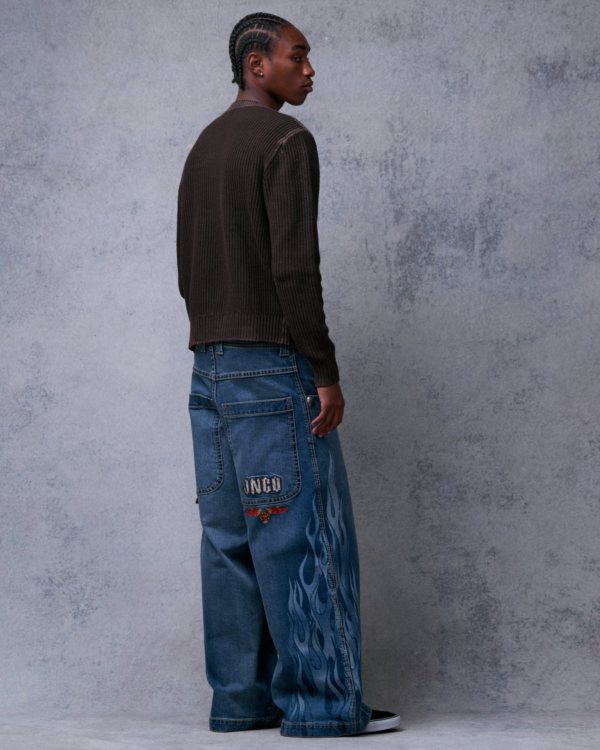 Model wearing wide-leg blue jeans with tonal flame print down the legs, rear three-quarter view showing back pocket