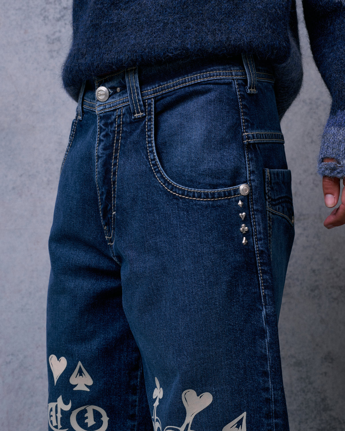 Close-up of the jeans' front waist and pocket with contrast stitching and card suit rivets below the pocket