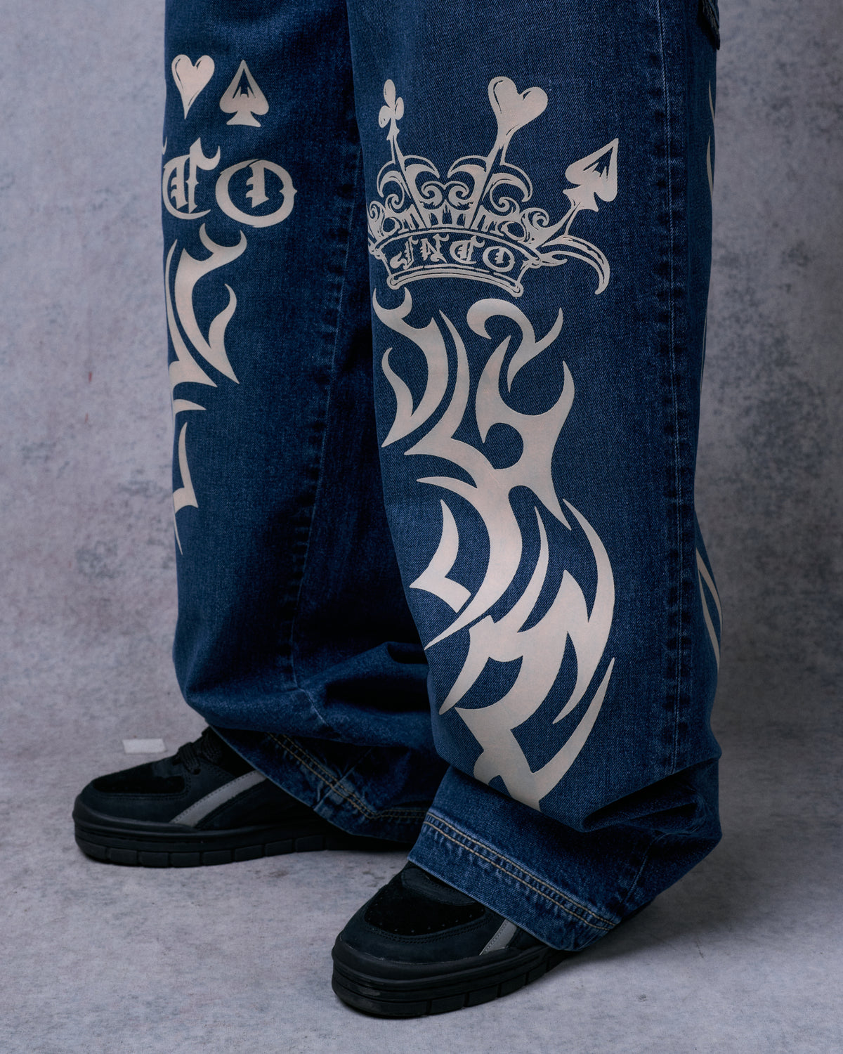 Close-up of the lower legs showing a cream crown and tribal graphic, wide hems over black sneakers