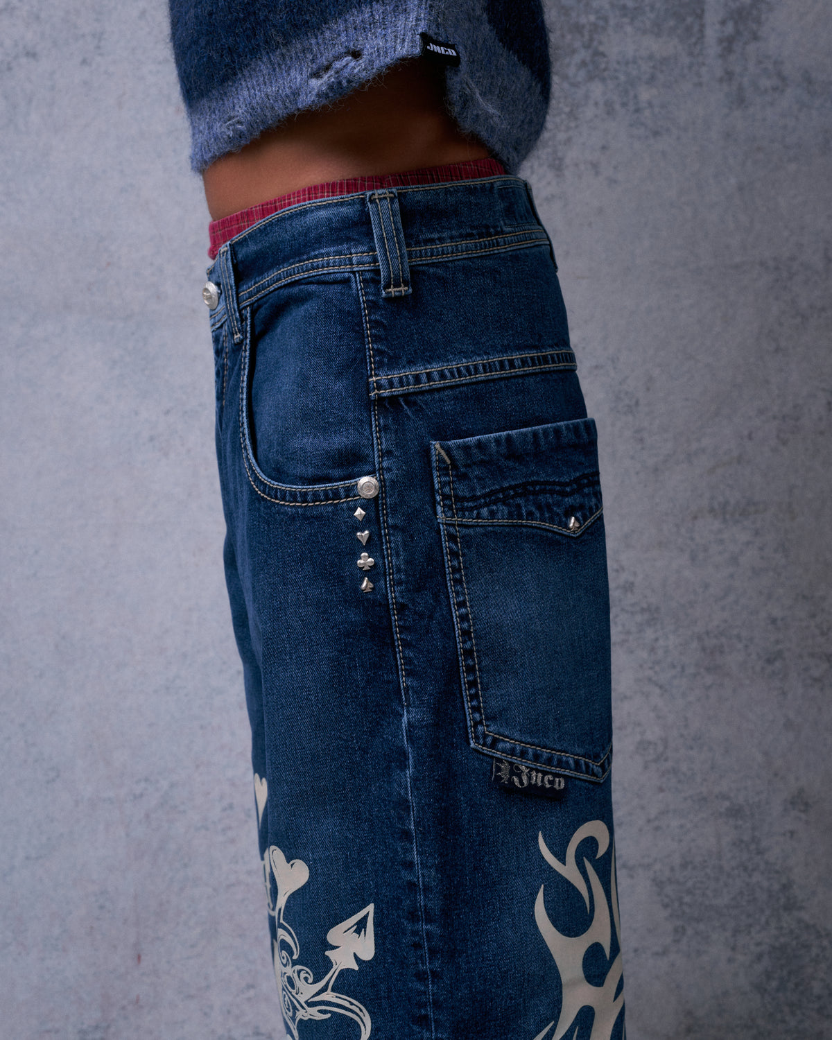 Side view of the jeans' hip showing card suit rivets, back pocket with logo tab and tribal graphics below
