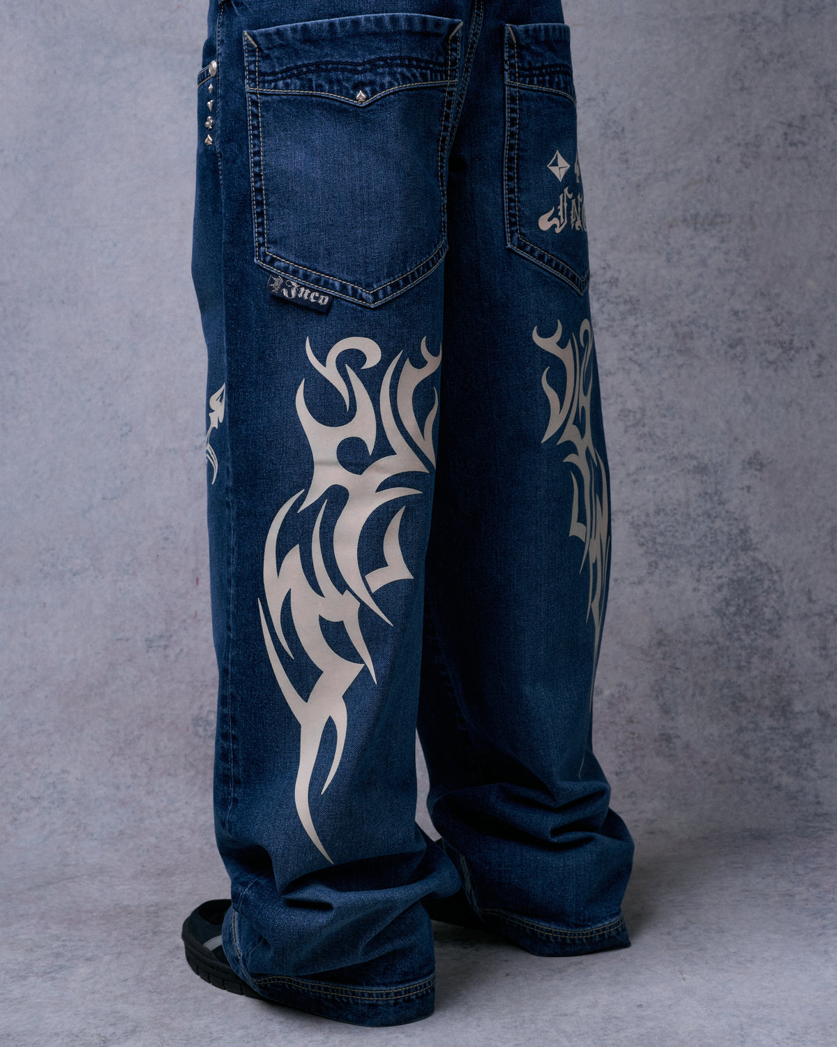 Back view of dark stone wide-leg jeans showing back pockets and cream tribal graphics down both legs
